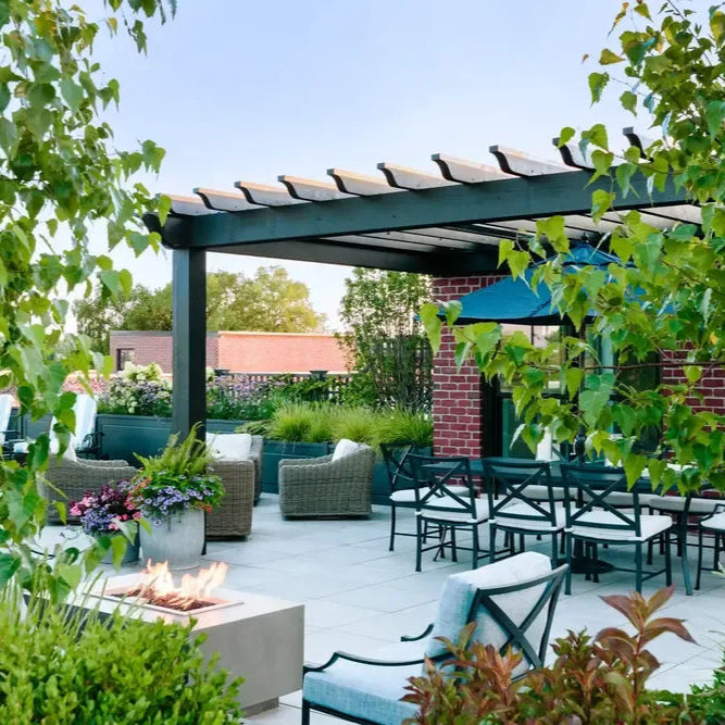 Outdoor patio with pergola, tables, chairs, and a fire pit surrounded by greenery.