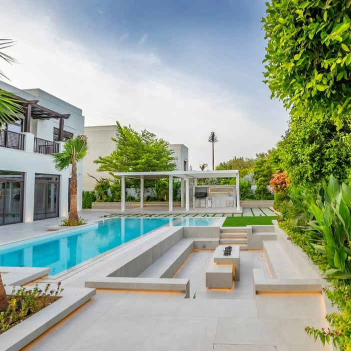 Modern pool area with lounge chairs, palm trees, and a house in the background.