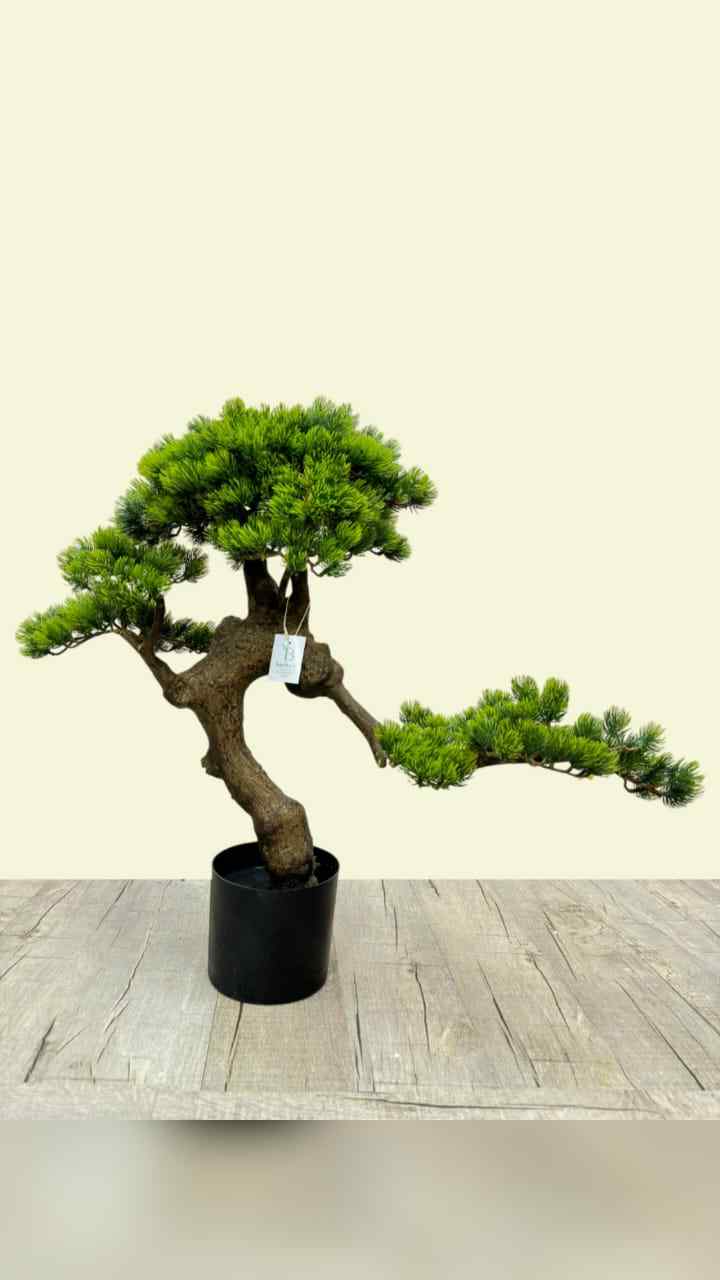 Artificial bonsai tree with green foliage and brown trunk in a black round pot