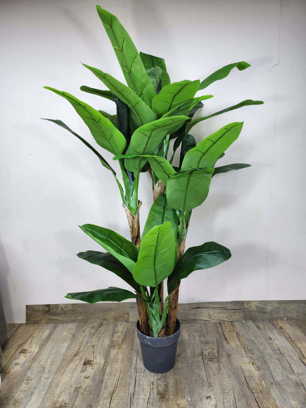 Artificial banana plant with green broad leaves in a gray plastic pot