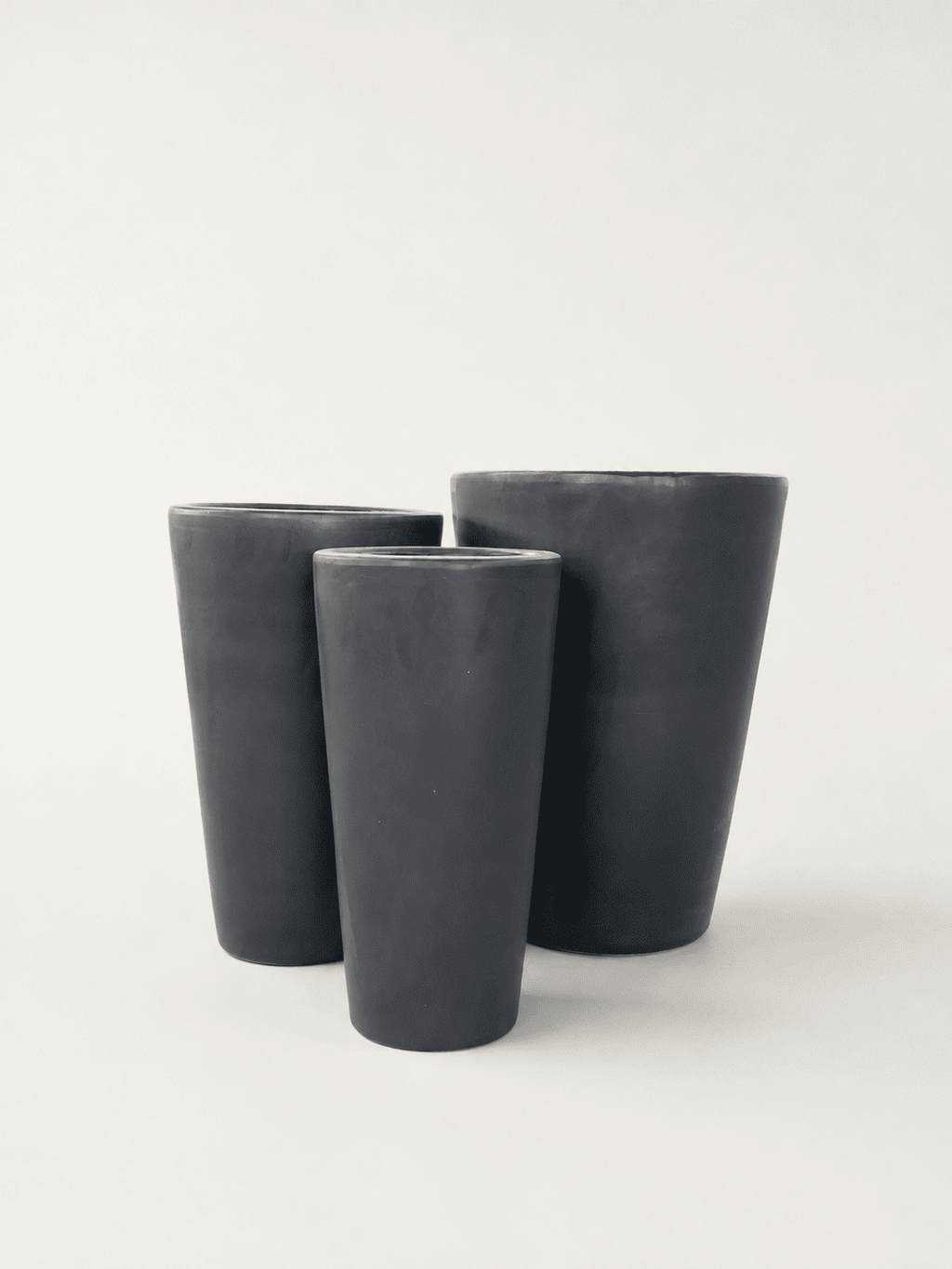Matte black ceramic tall planters, three stacked sizes, cylindrical shape.