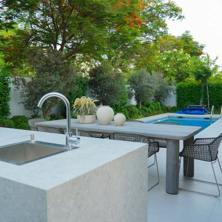 Outdoor kitchen area with sink, table, chairs, and pool in the background