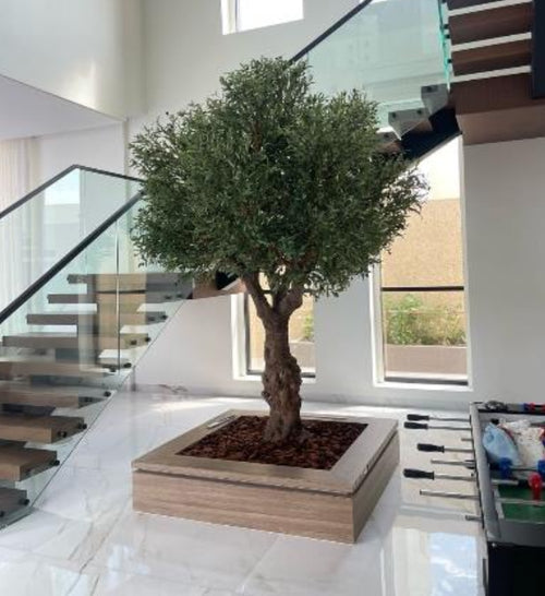 Artificial olive tree with green leaves in square wooden planter with dark soil