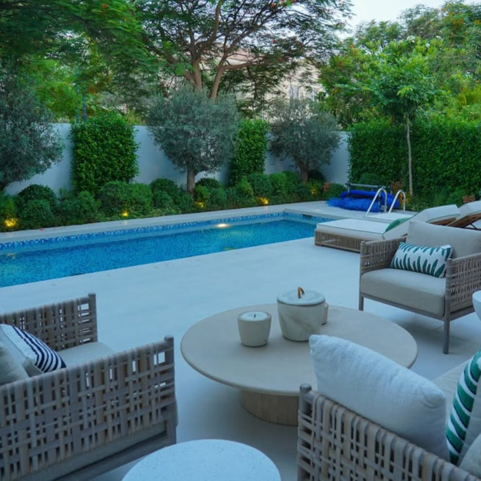 Outdoor patio area with pool, chairs, and table in a garden setting